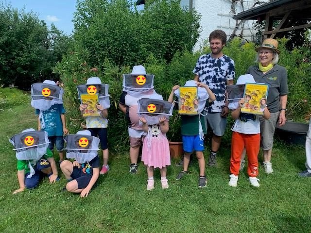 Kindergruppe mit Imkerschleiern und Broschüren im Garten der Imkerei Bertl