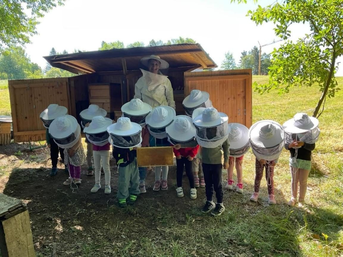 Kindergruppe mit Imkerschleiern vor einem Bienenhaus